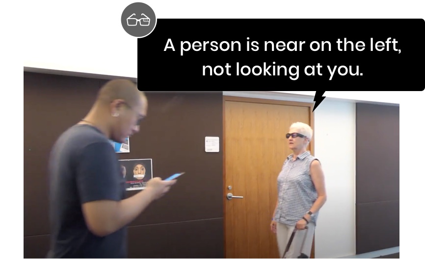 a blind users wearaing smart glasses is about to pass by a passerby who is looking at the phone. The smart glasses provided speech feedback, which says 'a person is near on the left, not looking at you.'