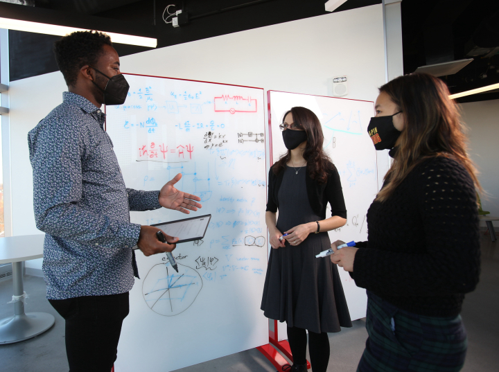 photo of Undergraduate physics major Jade LeSchack (right in photo) discusses quantum information science with QuICS Fellow Nicole Yunger Halpern (center) and physics graduate student Anthony Munson (left).